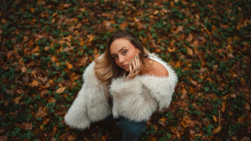 Professional portrait by Elliot Aubin using the Sigma 35mm F1.4 DG DN Art lens. A model in a white fur coat poses in a forest of autumn leaves, showcasing the lens's signature bokeh, sharp subject separation, and premium optical performance. Available via Sigma Pakistan official channels and Hope Enterprises.